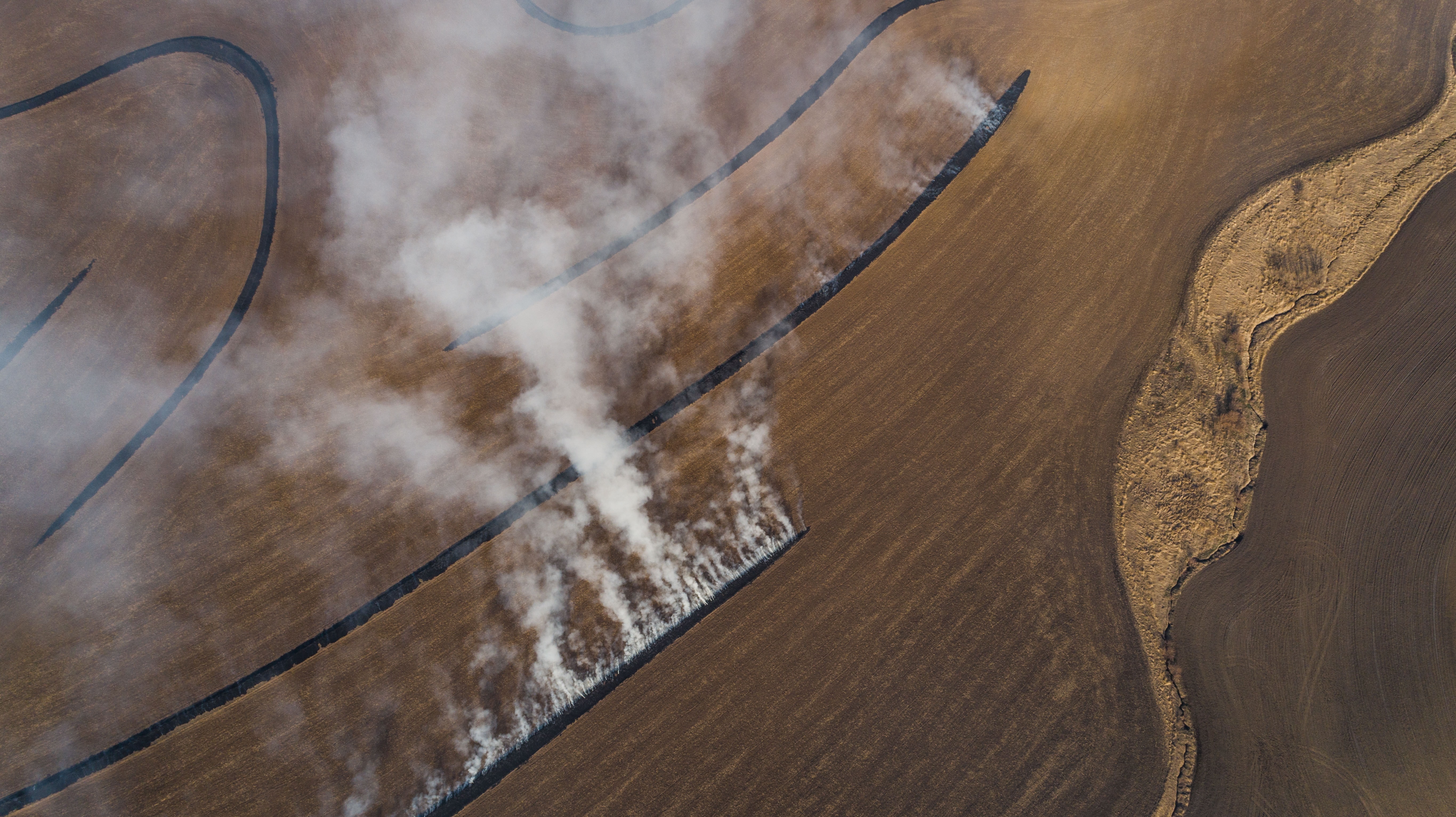 A field is seen from above with fire burning in specific lines 