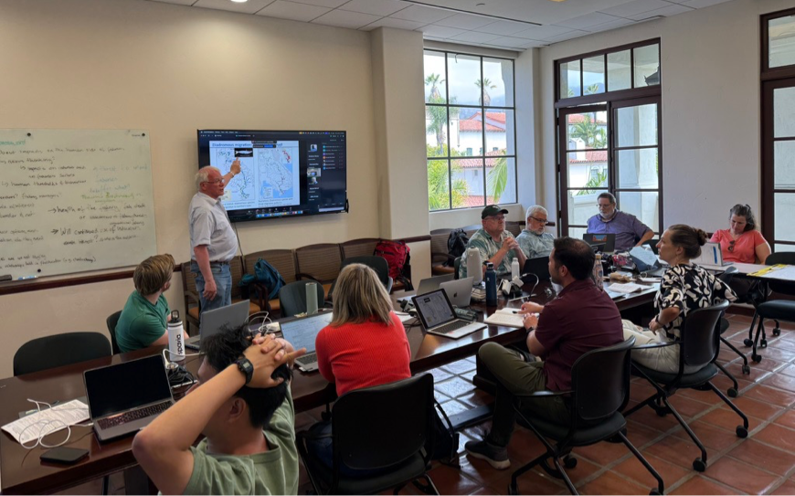 GO FISH member presents a map to a group seated at a large table. They have laptops and are in discussion.