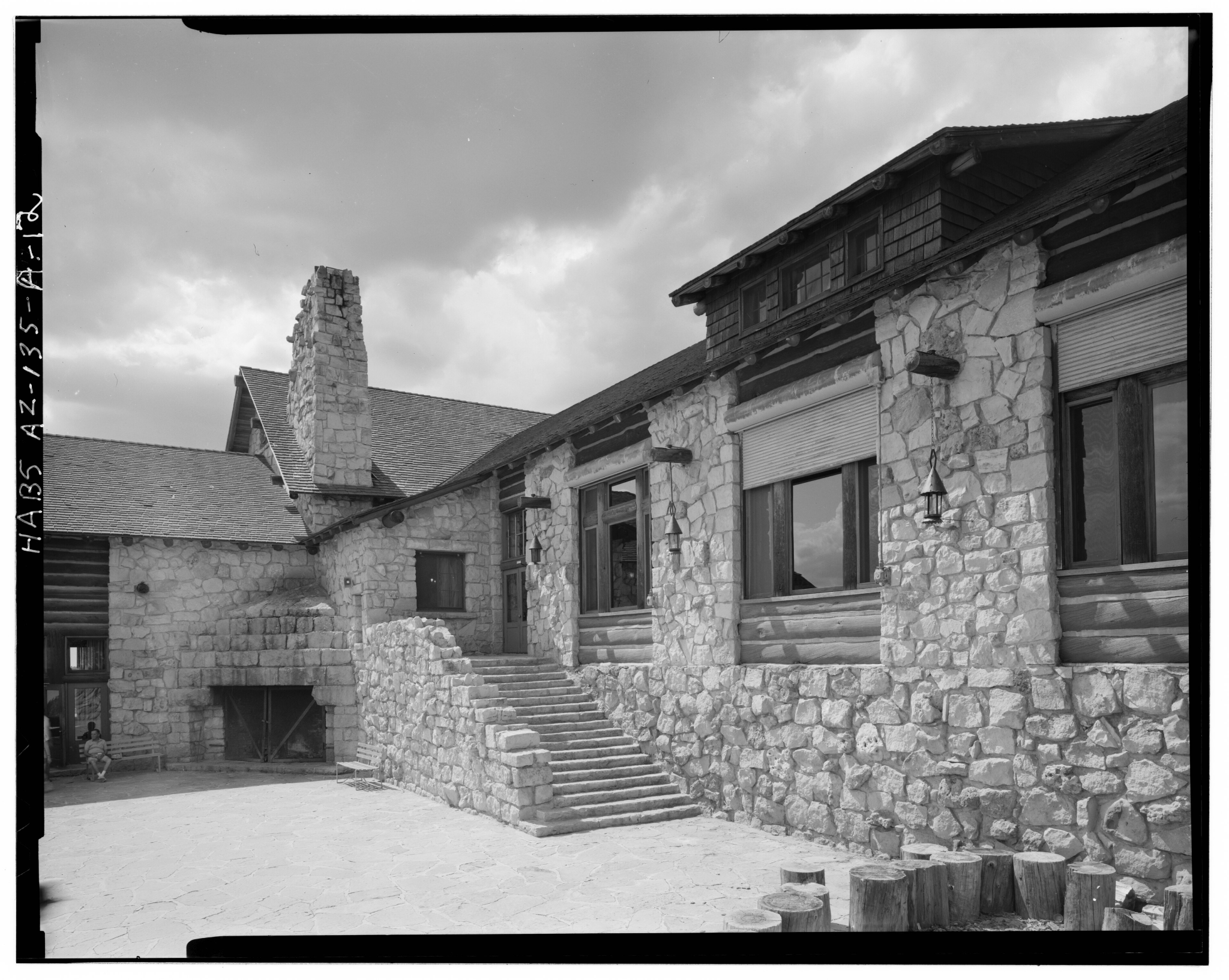 A rustic stone building with a prominent chimney and steps leading to a large windowed entrance, set against a cloudy sky.