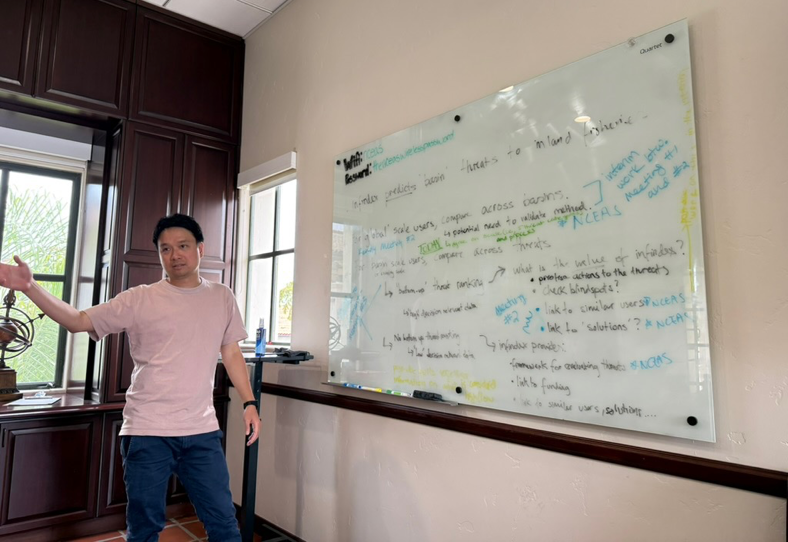 Working group member stands in front of a white board filled with data, presenting what is there.