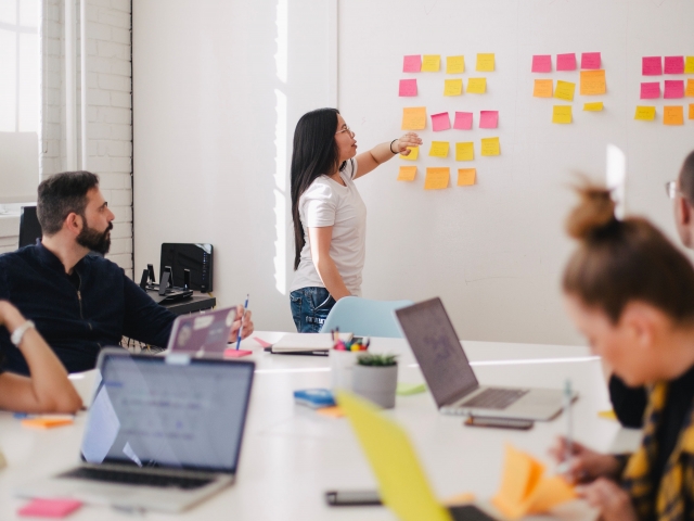 Woman using sticky notes on a white board, group watches