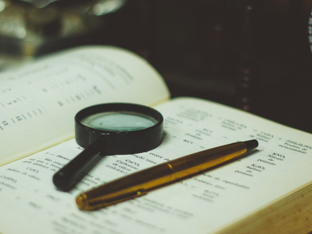 magnifying glass and pen on top of a book