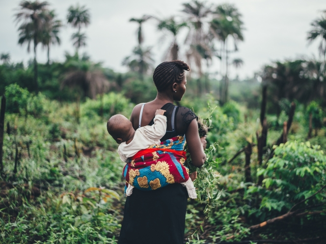 Mother carries child on back in tropical forest