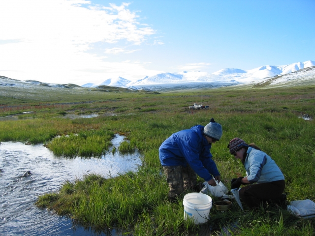 Two female researchers taking samples and mountains in background
