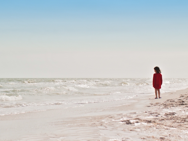 Young girl in red dress standing on beach