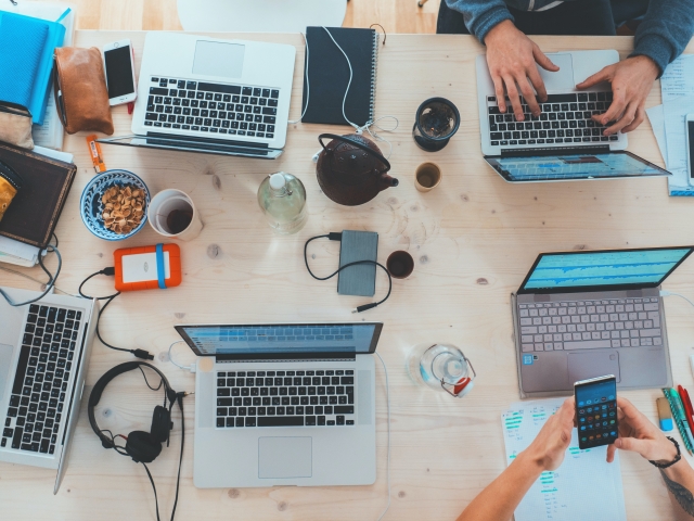 Table with multiple open laptops, cables and phones.