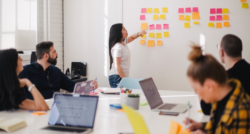 Woman using sticky notes on a white board, group watches