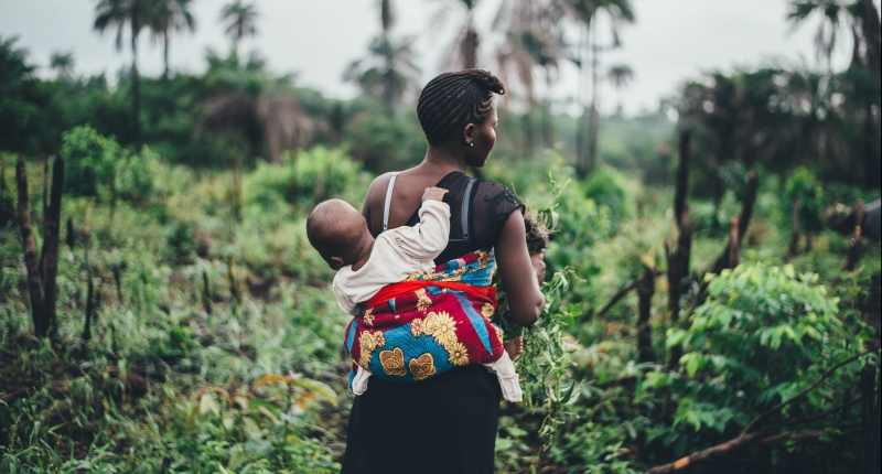 Mother carries child on back in tropical forest