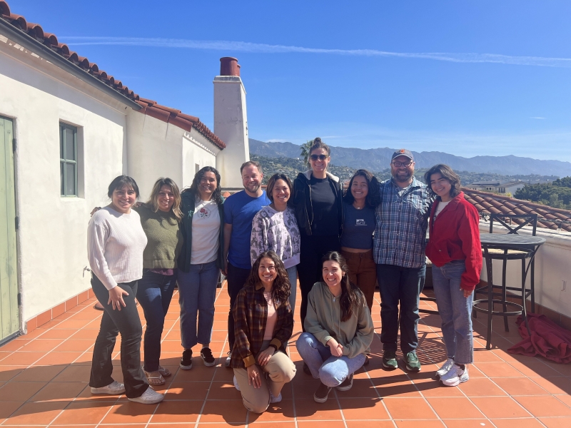 Group of nine coreR participants and two instructors gathered in two rows smiling for a group photo on the NCEAS terrace with the Santa Ynez Mountains in the background