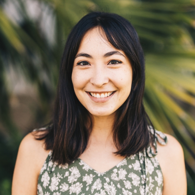 A headshot of Cristina outside by green palm fronds 